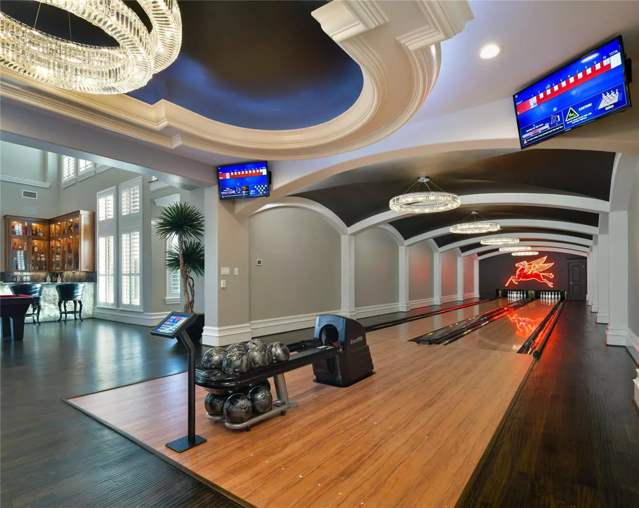 Private two-lane bowling alley connected to a luxury home's entertainment area with elegant tray ceilings and crystal chandeliers.